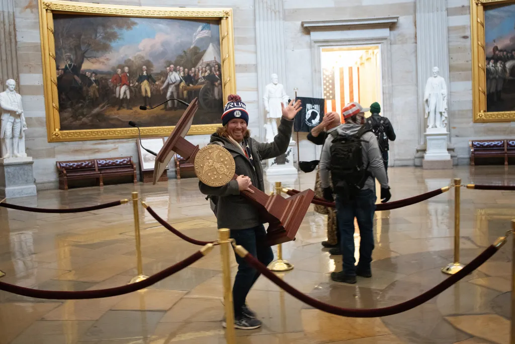 A man wearing a "Trump 45" hat carries the Speaker of the House podium, showing its gold seal.