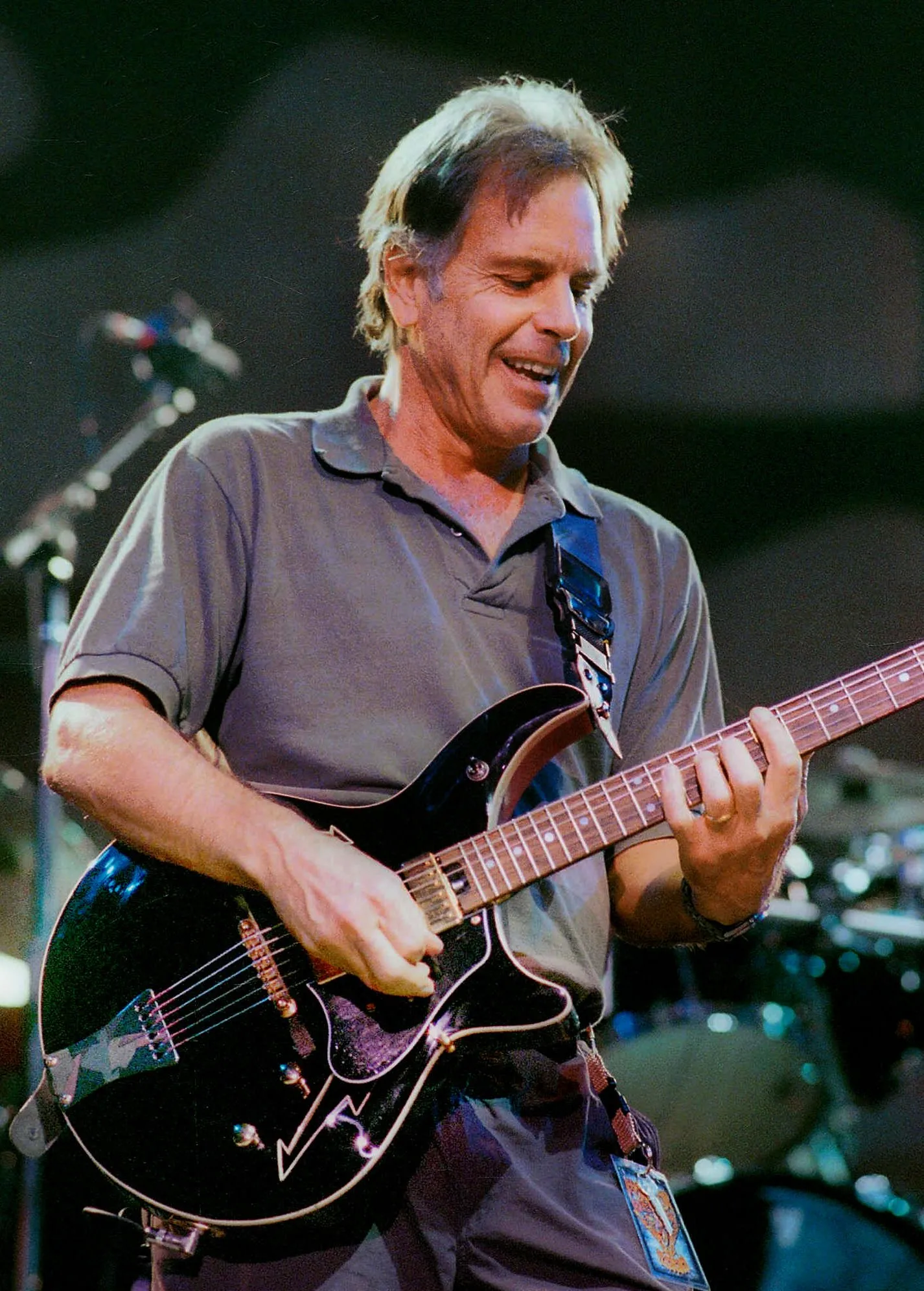 Bob Weir smiling and playing a black electric guitar.