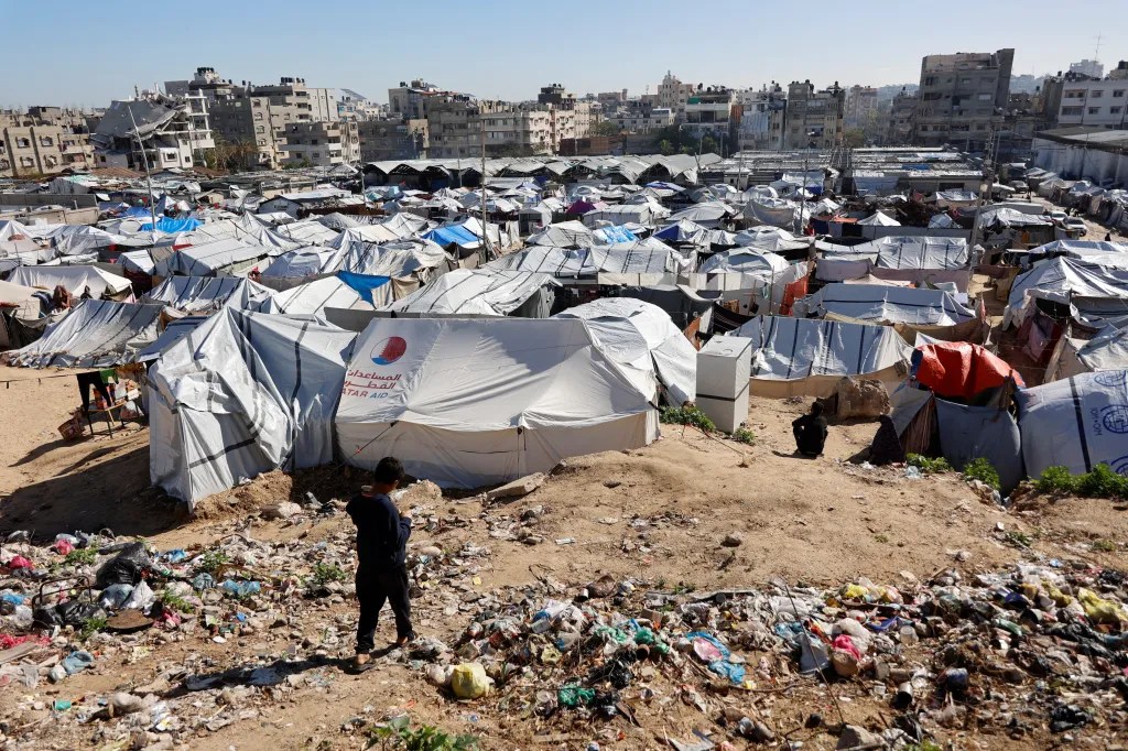 A child walks past a mound of garbage toward tent shelters for displaced Palestinian families in Gaza City.