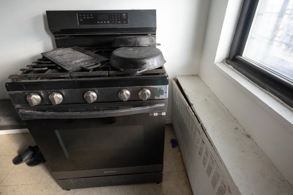 A dirty, broken black stove and a broken white radiator with a window above it.