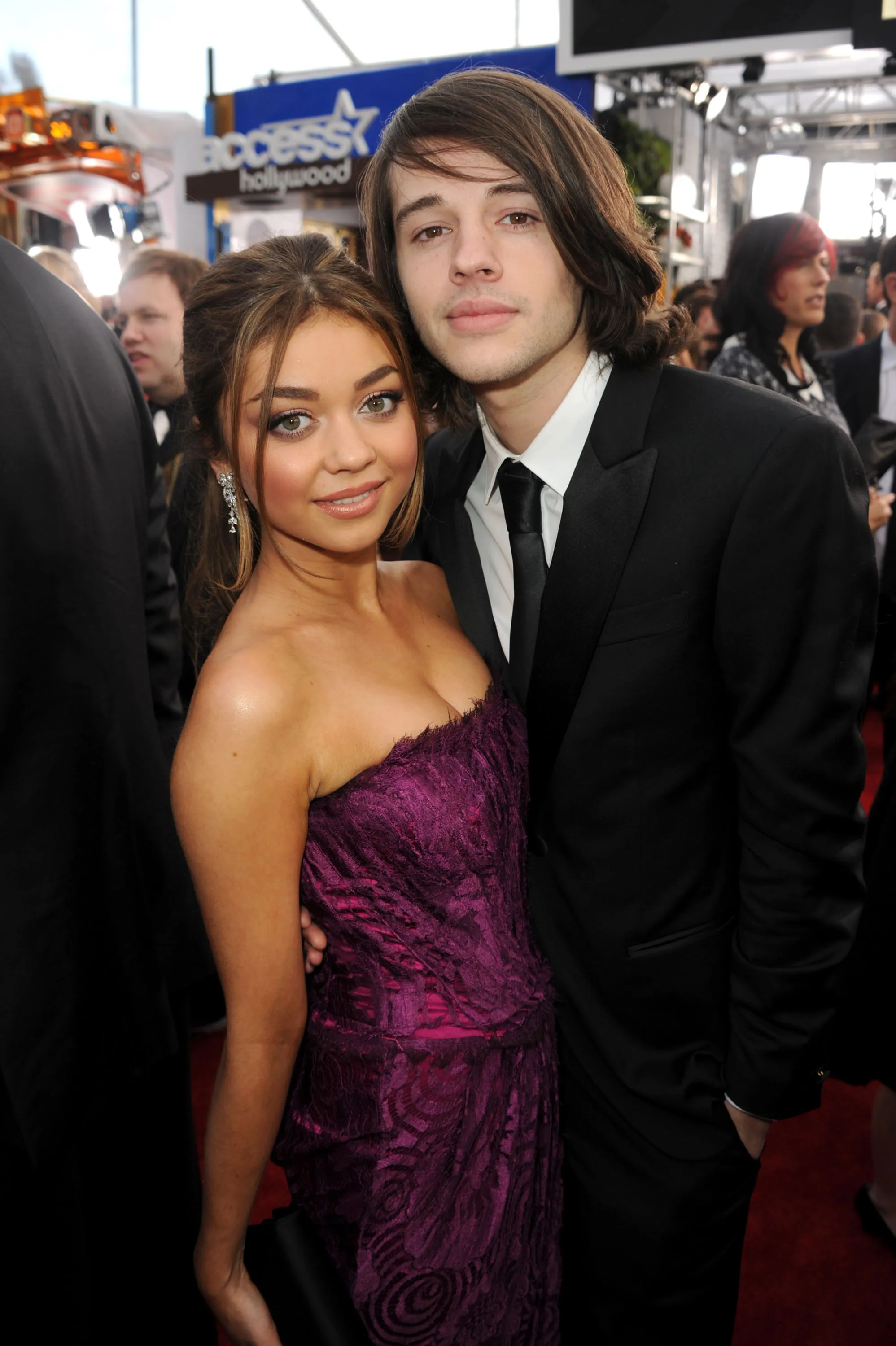Sarah Hyland in a purple strapless dress and Matt Prokop in a black suit pose on a red carpet.