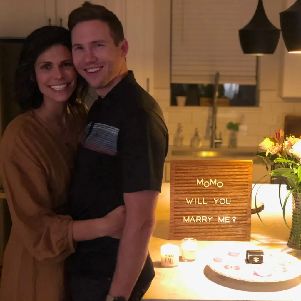 Spencer and Monique Tepe posing for a photo with a "Momo will you marry me?" sign in the background.