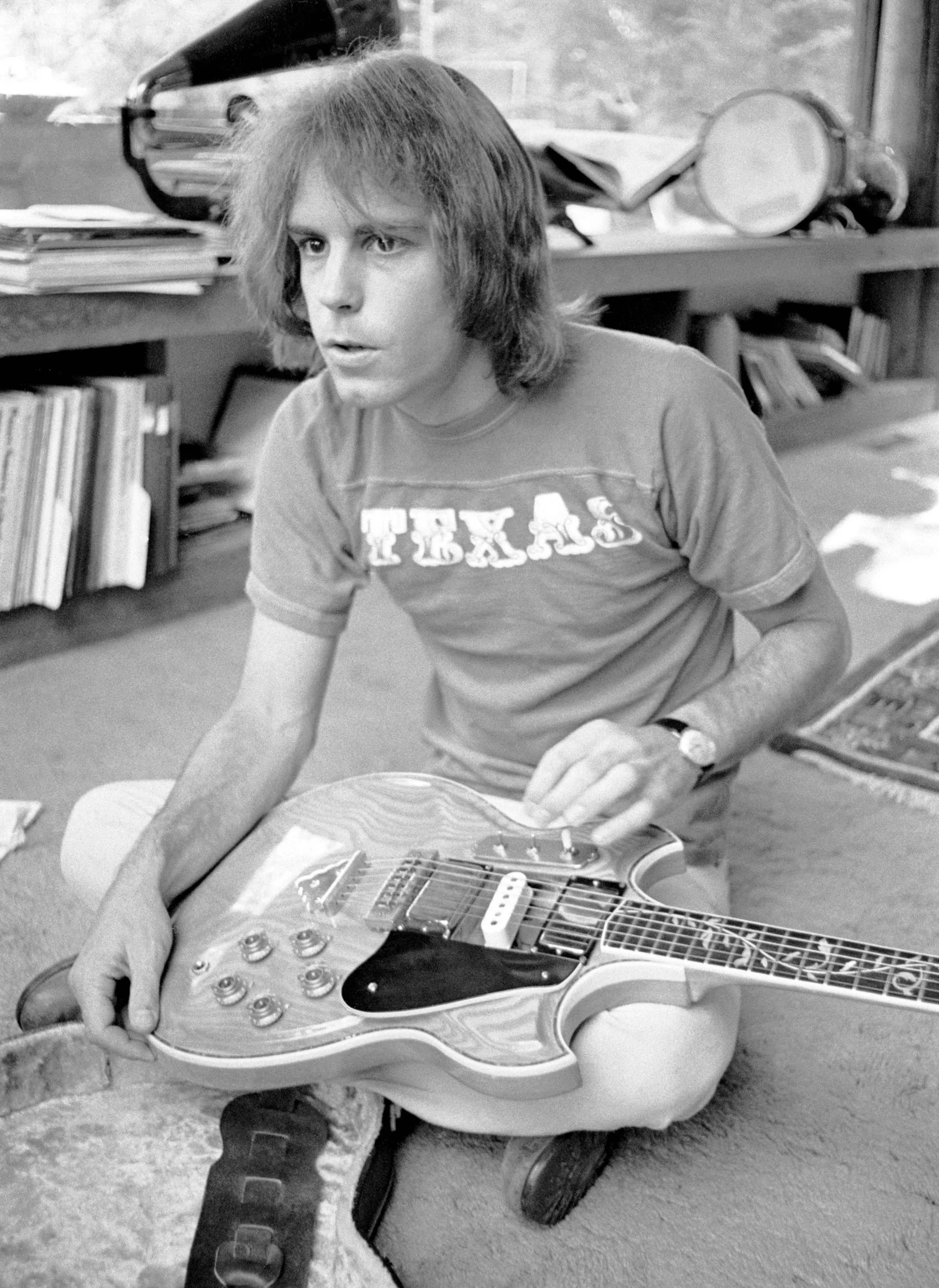 Bob Weir of Grateful Dead tuning his guitar while sitting on the floor.