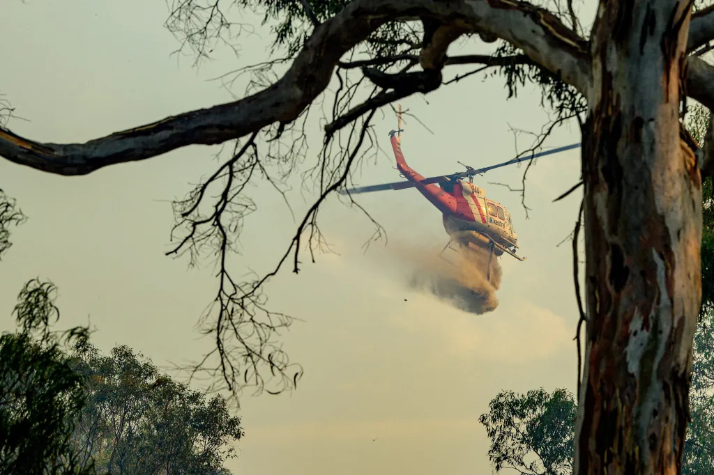 A red and white firefighting helicopter drops water over a bushfire.