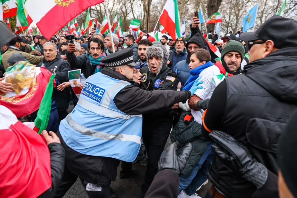 Police officer scuffles with Iranian protesters holding flags.
