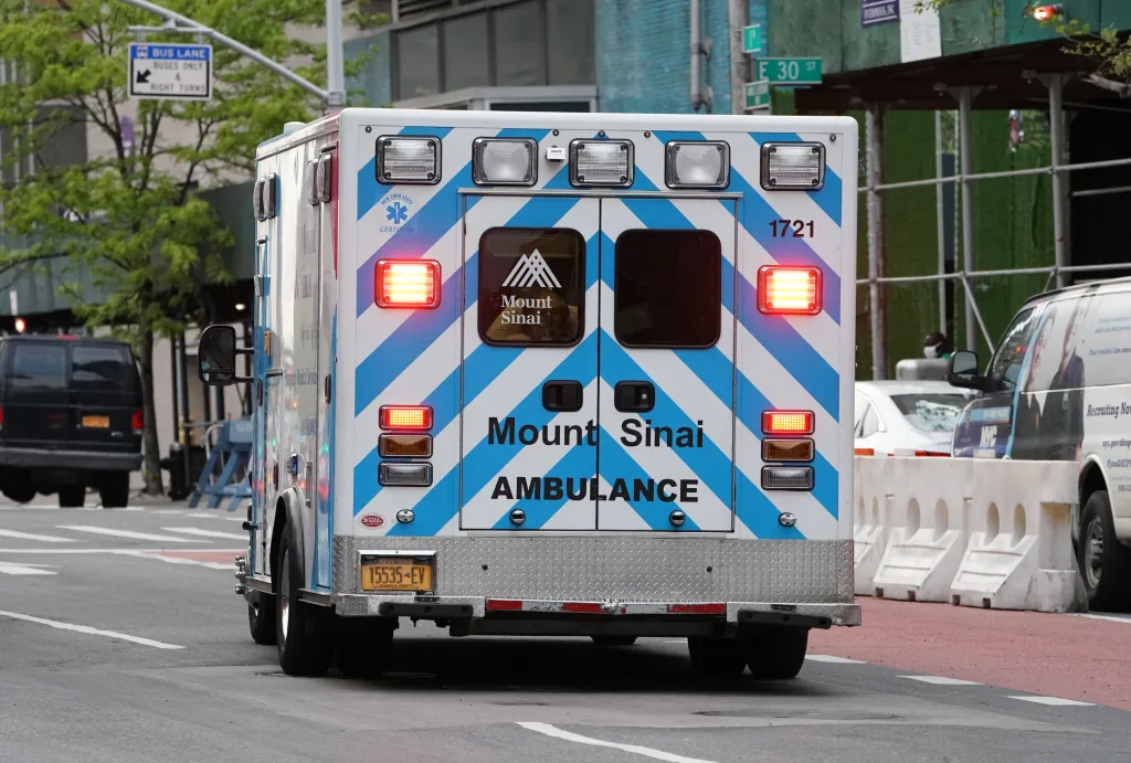 Rear view of a Mount Sinai ambulance with flashing lights driving on a city street.