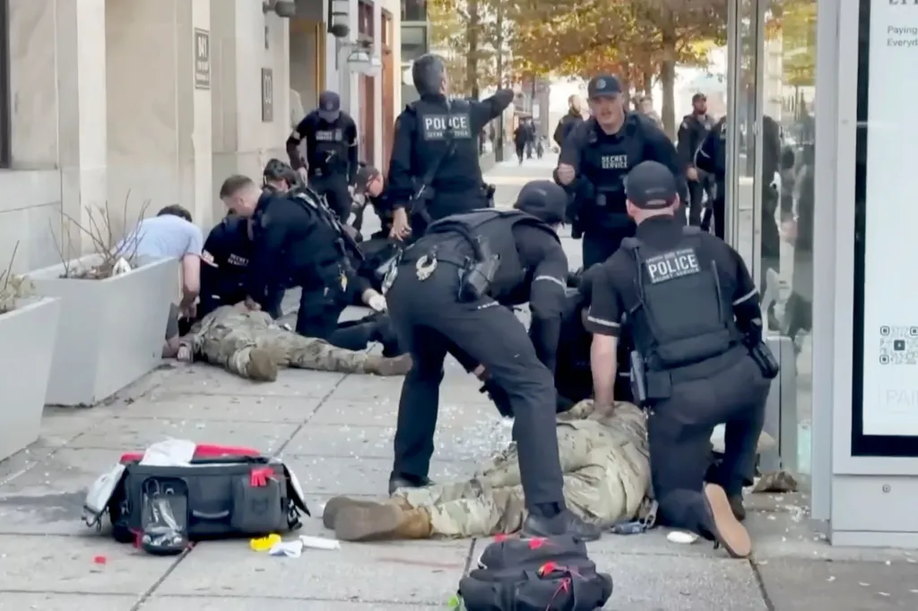 Secret Service officers and other individuals tending to two National Guard soldiers lying on the ground on a sidewalk.