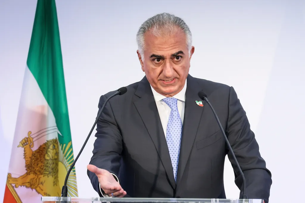 Reza Pahlavi speaking at a news conference, with the Iranian flag behind him.