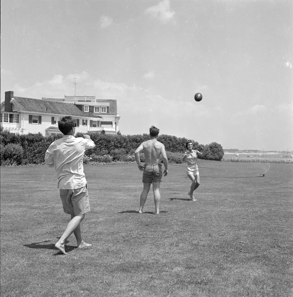 Senator John F. Kennedy, Jacqueline Bouvier, and Edward Kennedy play football on the lawn of the Kennedy compound.