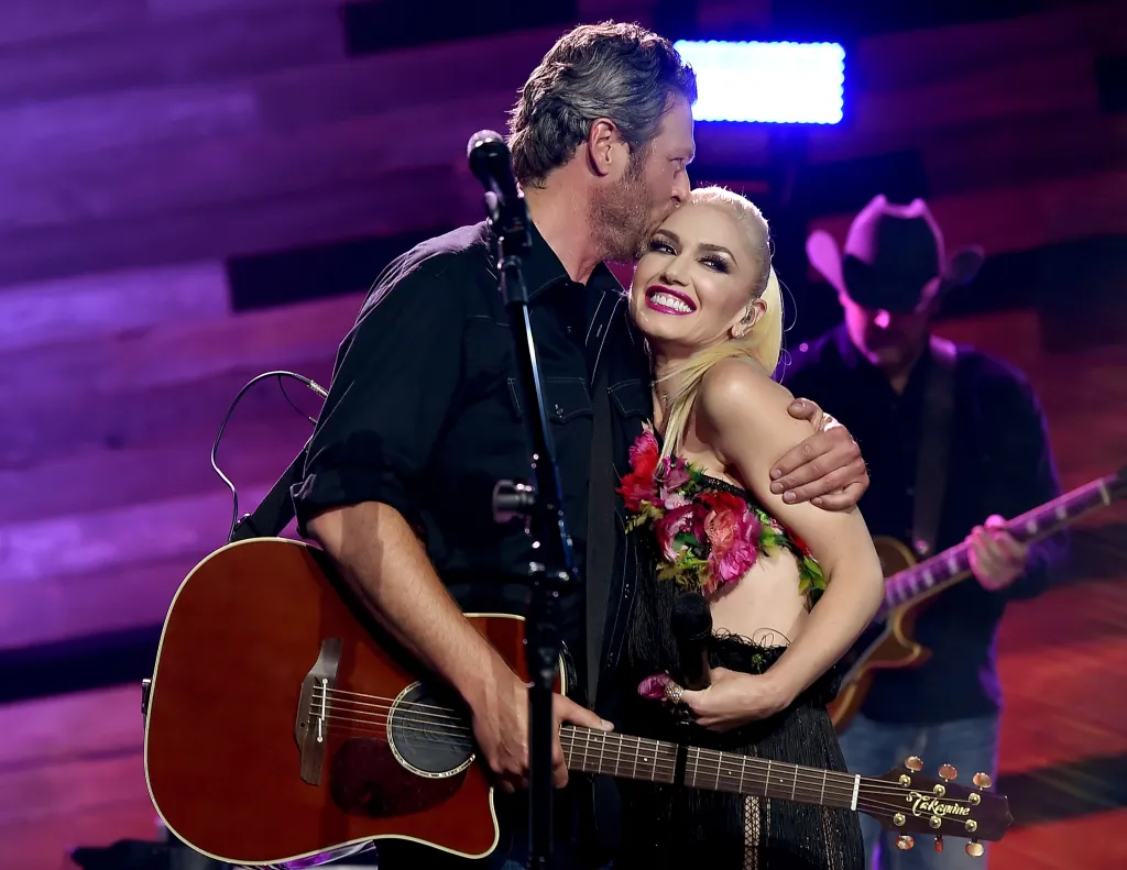 Blake Shelton kissing Gwen Stefani on the forehead while both perform on stage.