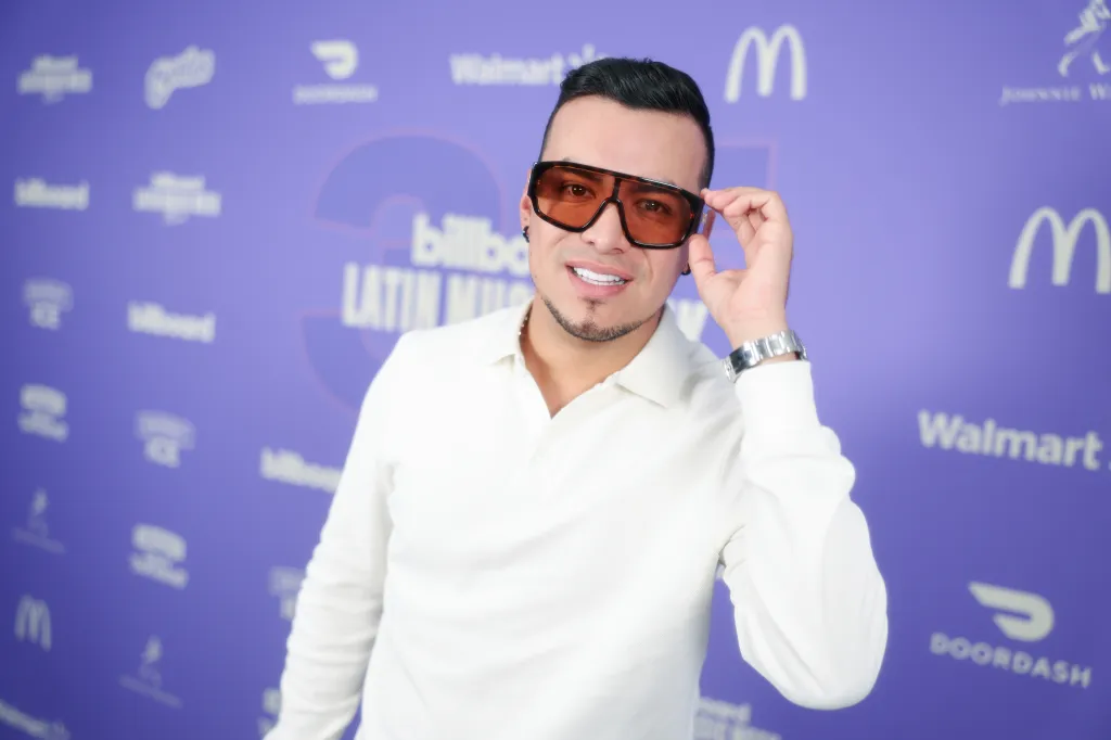 Yeison Jimenez adjusting his sunglasses, posing in front of a purple backdrop with "Billboard Latin Music Week" and various sponsor logos.