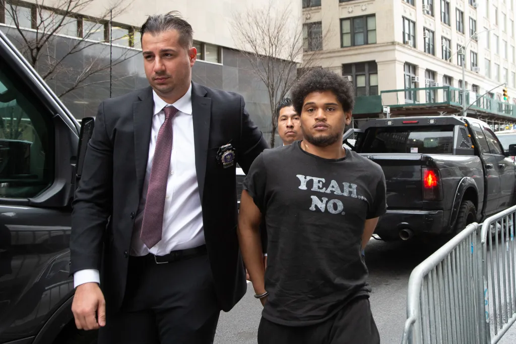 Halley Tejada, 19, in a "YEAH NO" t-shirt, handcuffed, escorted by an officer in a suit.
