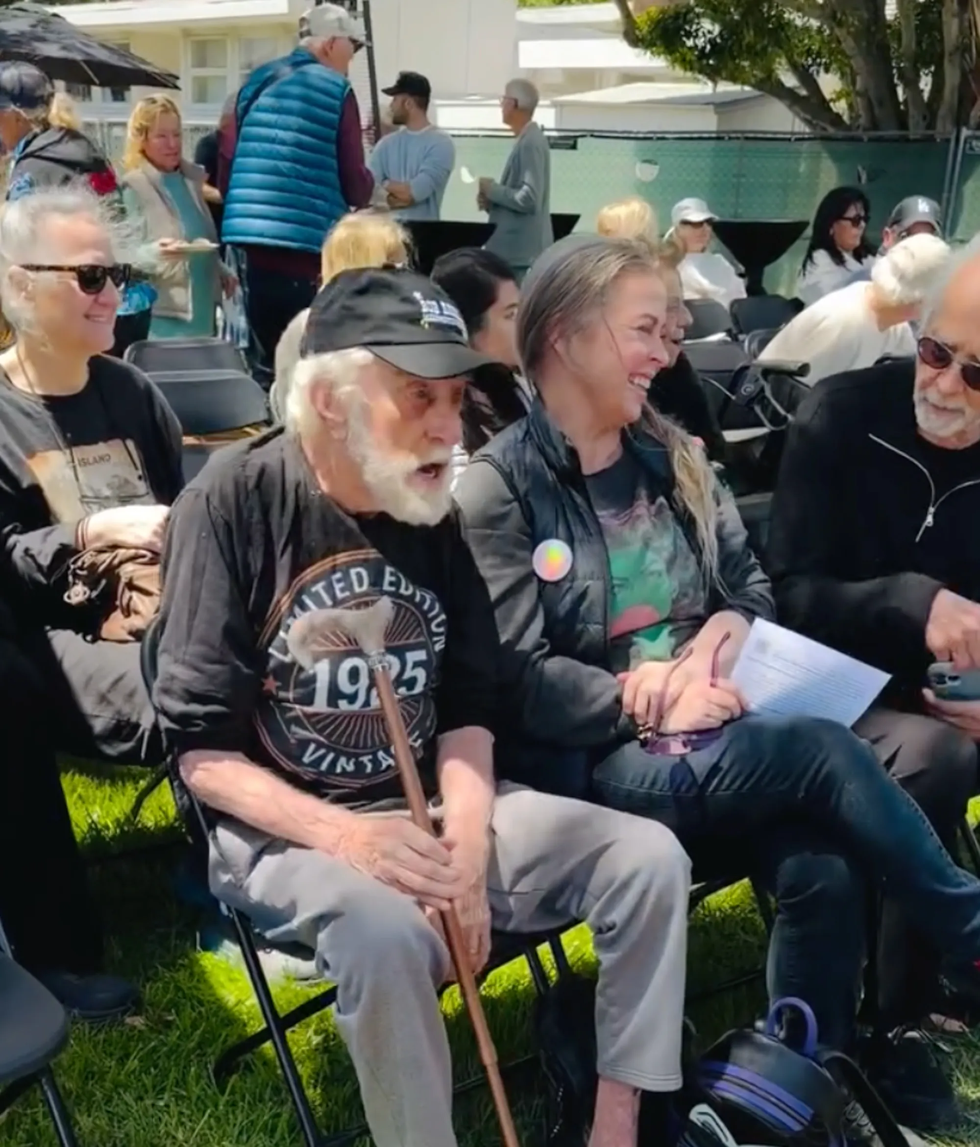 Dick Van Dyke, wearing a black baseball cap and a black t-shirt, sits next to his wife, Arlene Silver, at a Malibu event.