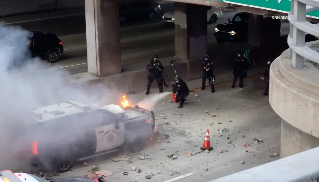 Law enforcement officers attempt to extinguish a fire on a California Highway Patrol vehicle.
