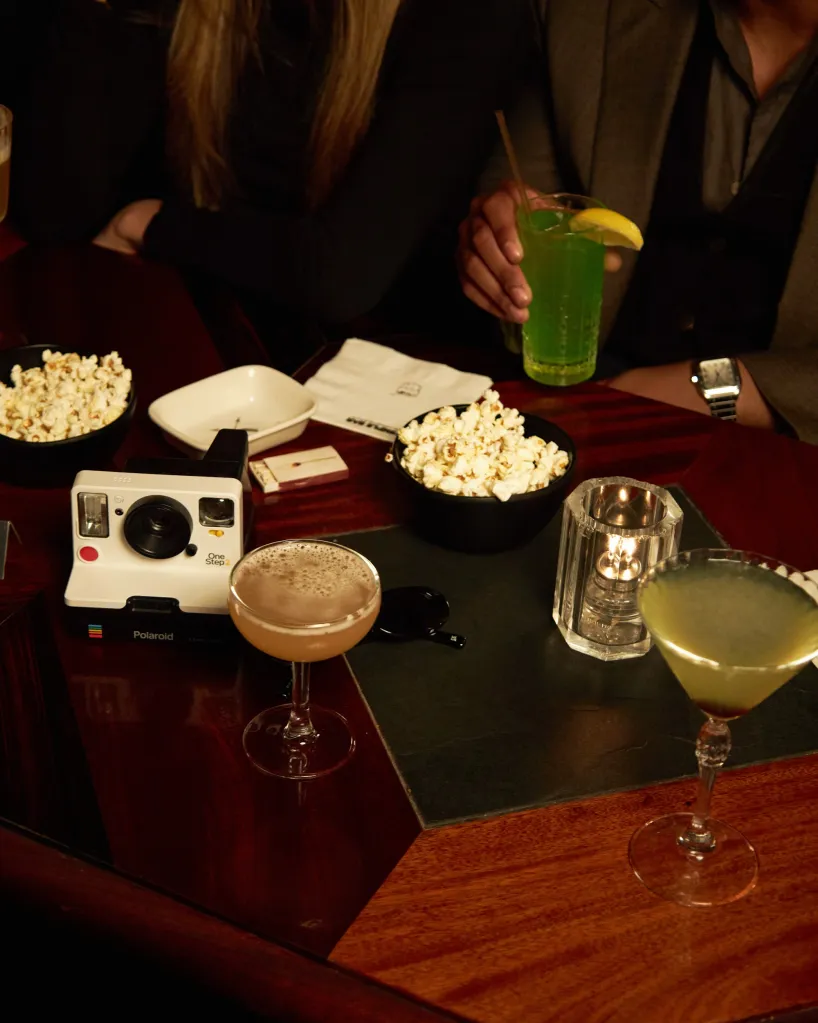 A table with popcorn, cocktails, and a vintage camera, with two people in the background.