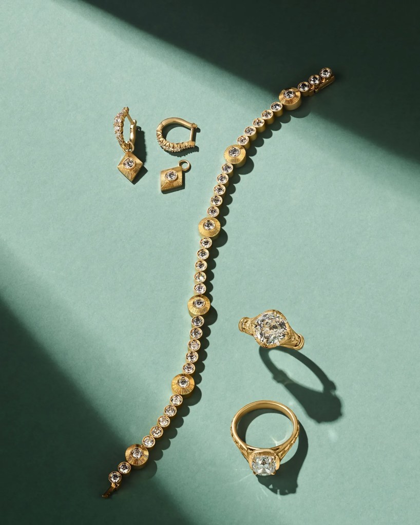 A gold diamond bracelet, a gold ring with a single diamond, a pair of gold diamond earrings, and a small gold diamond pendant on a blue-green background.