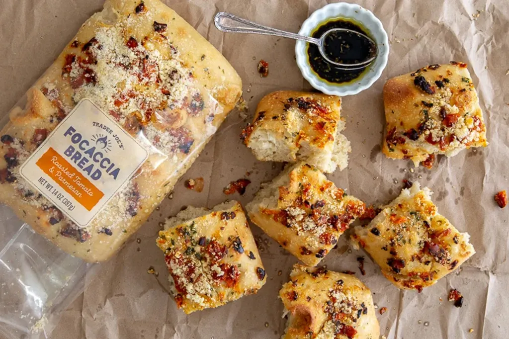 Trader Joe's Focaccia Bread with roasted tomato and parmesan, with several pieces torn off, next to a small bowl of olive oil and balsamic vinegar.