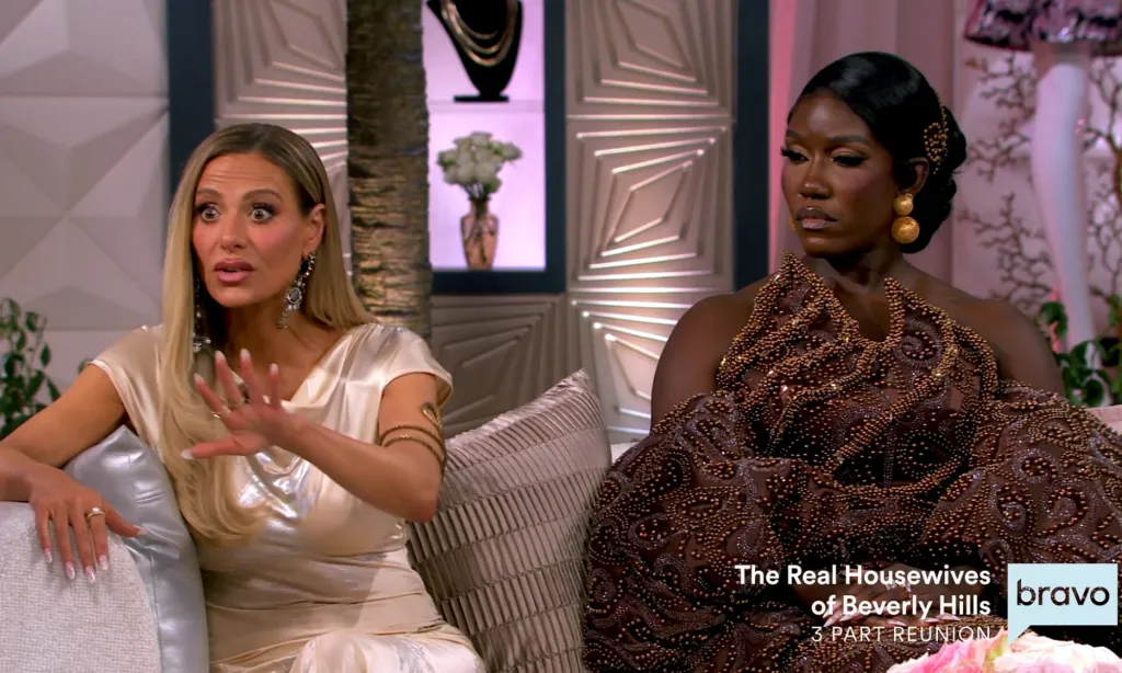 Two women sitting on a couch, with one woman gesturing and the other looking off-camera.