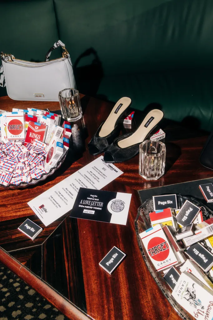 A white Nine West purse, black Nine West heels, a menu, and various candies are scattered on a table.