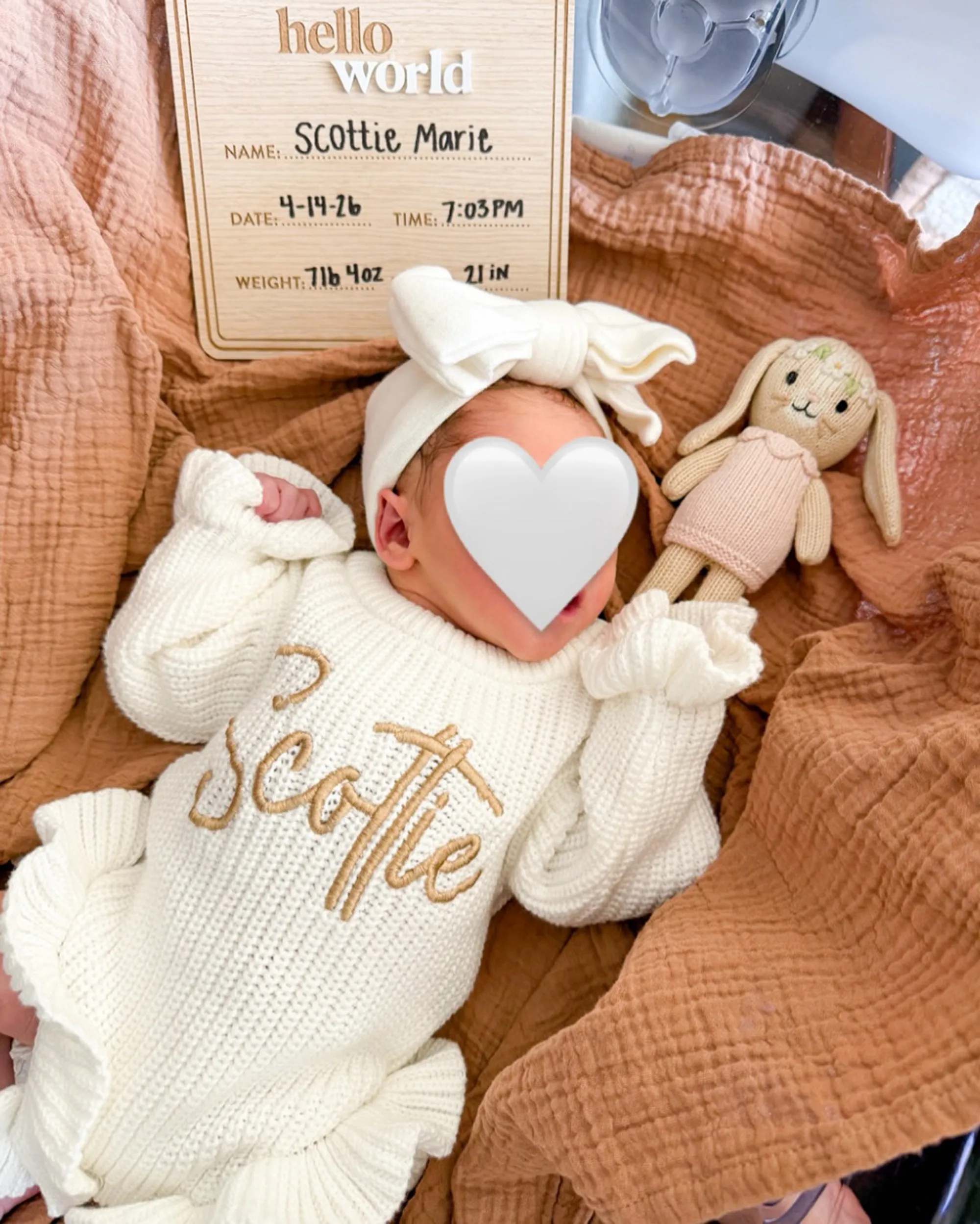 A newborn baby, Scottie Marie, wearing a white knitted outfit and headband, lies next to a knitted bunny and a "Hello World" wooden plaque detailing her birth information.
