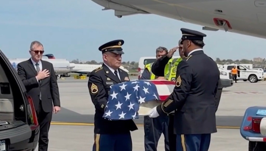 Military personnel carrying a flag-draped casket from an airplane.