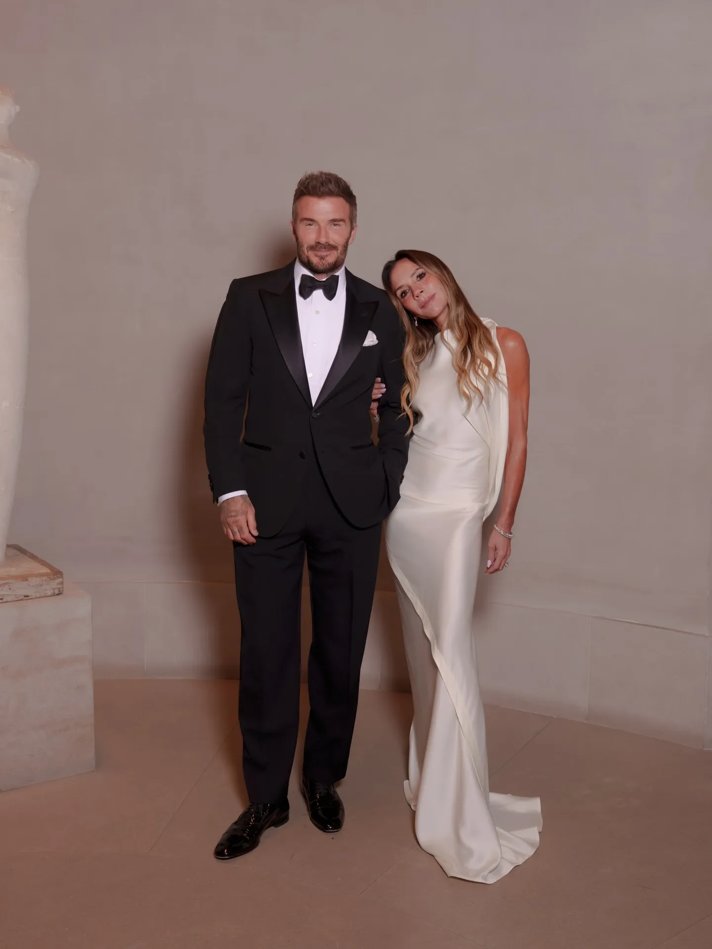 David and Victoria Beckham in formal attire, Victoria with her head resting on David's shoulder.