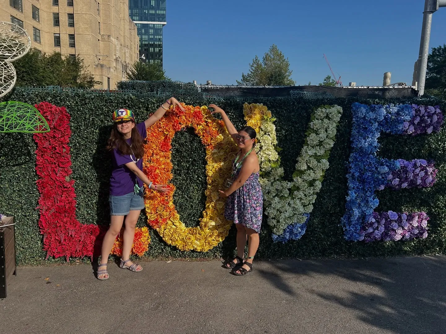 Tina Zhu Xi Caruso and Pari Kim posing in front of a flower display that spells "LOVE".