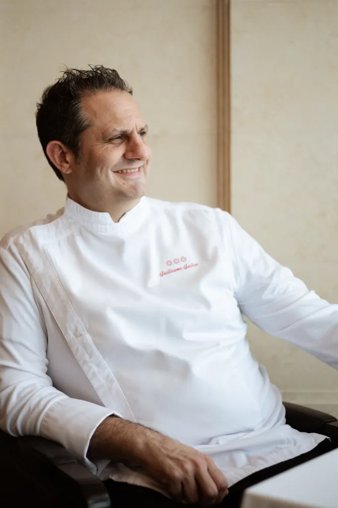 Guillaume Galliot smiling, wearing a chef's jacket with his name embroidered on it.