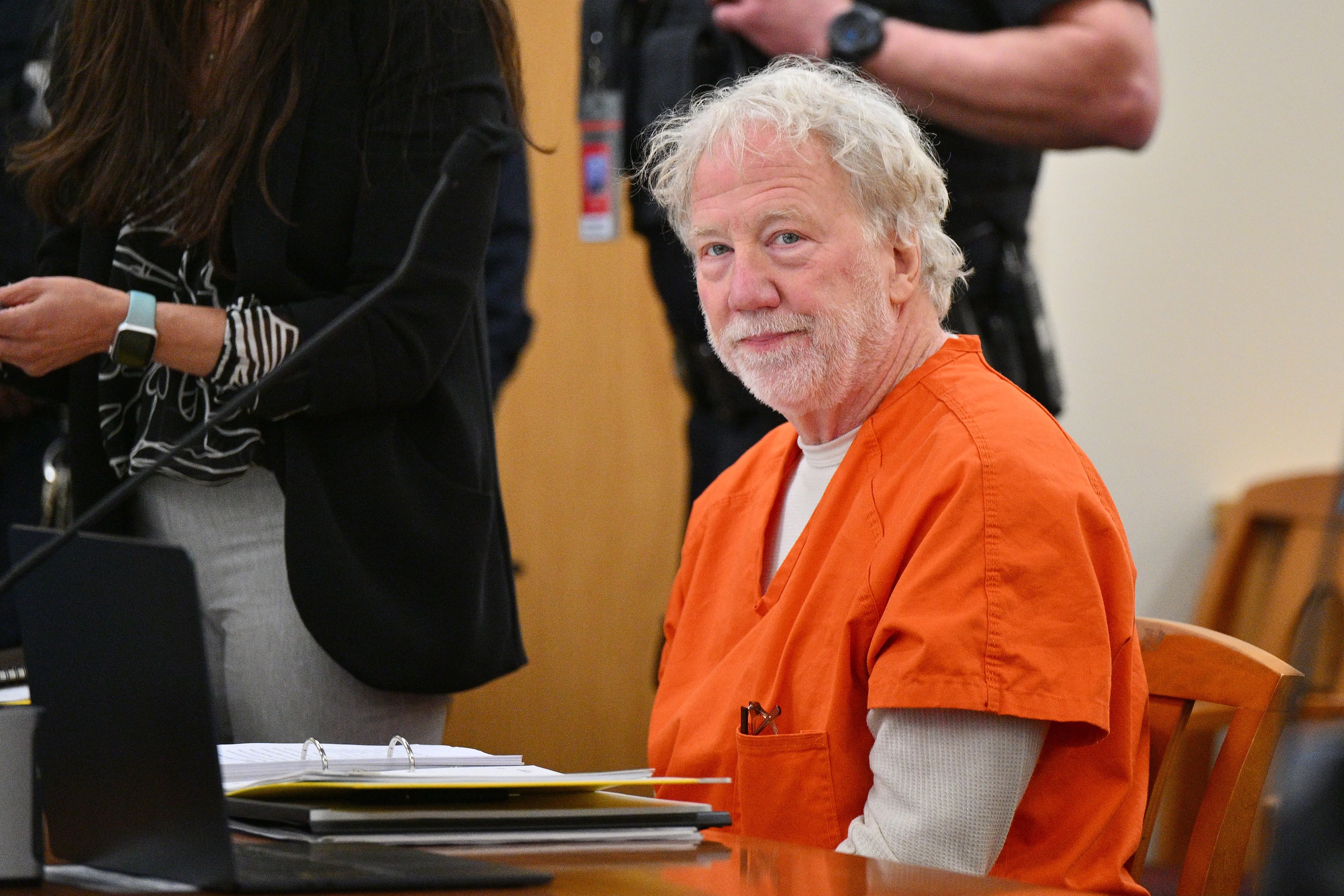 Timothy Busfield in an orange jumpsuit looks at the camera during a hearing in court.