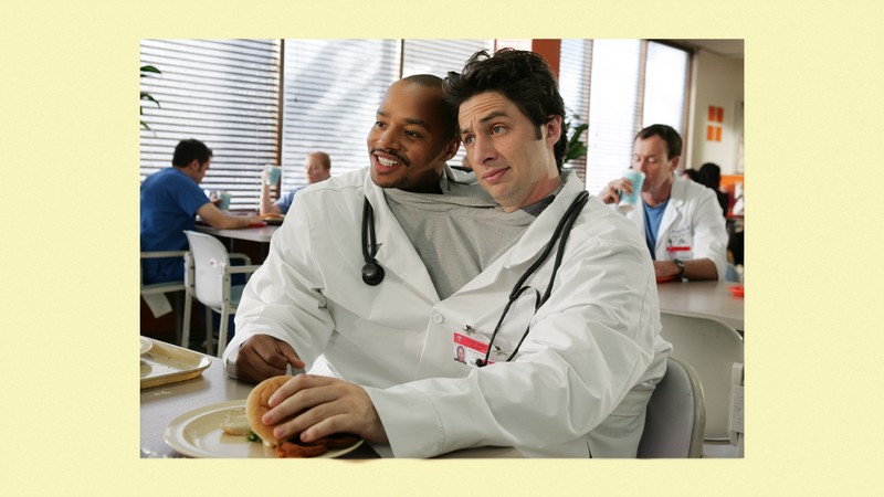 Donald Faison and Zach Braff sharing a single shirt and doctor's jacket, in a scene from 