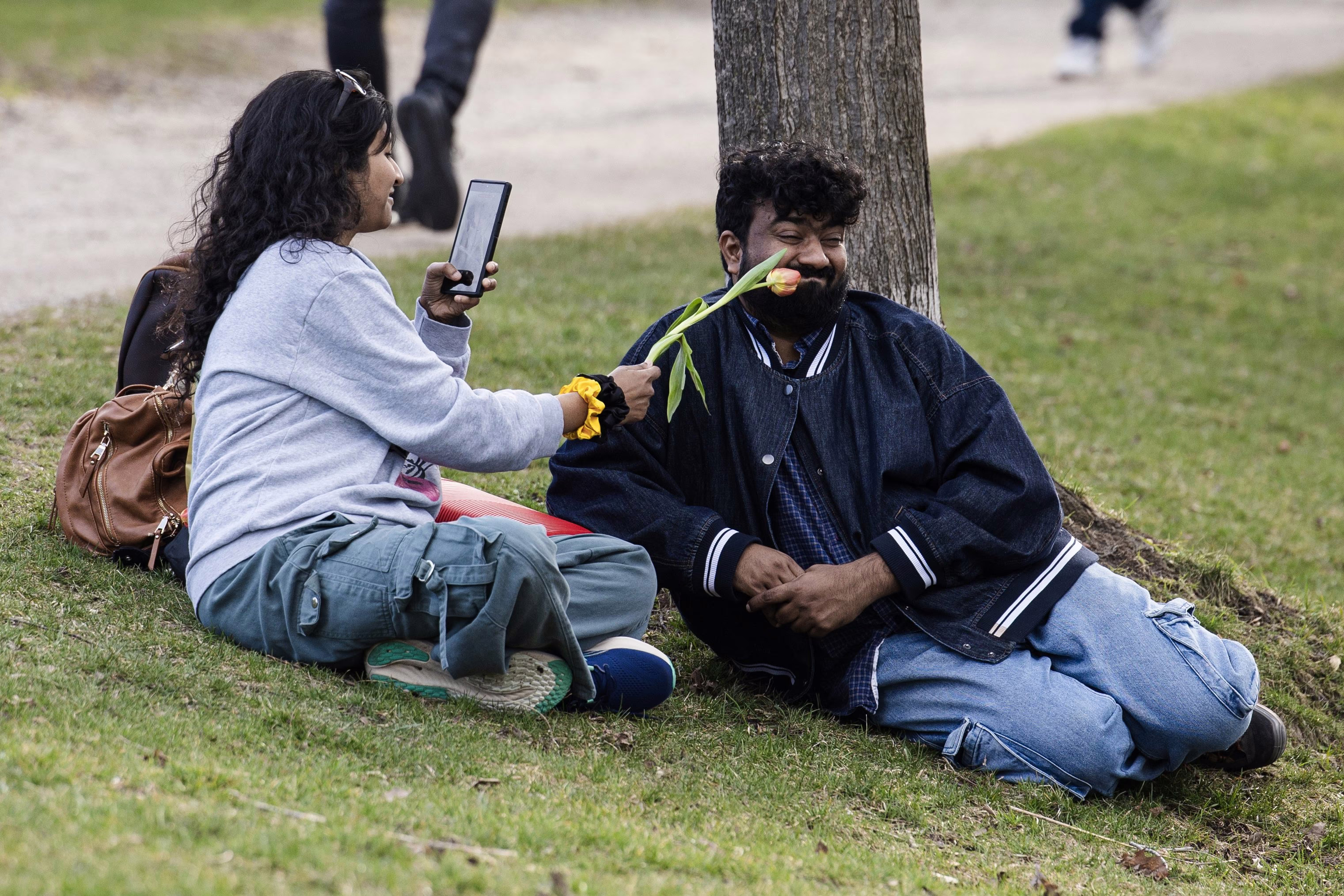A woman teases her husband with a tulip while sitting in a park.