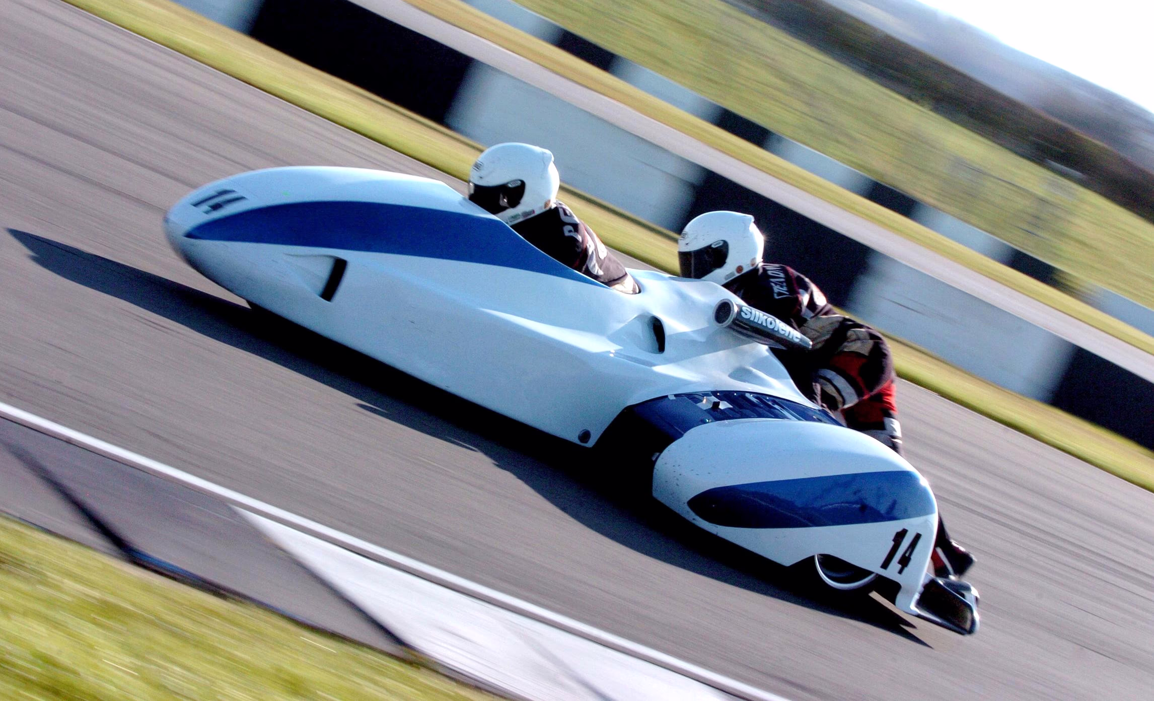 Two people ride a streamlined motorcycle-and-sidecar in a race.