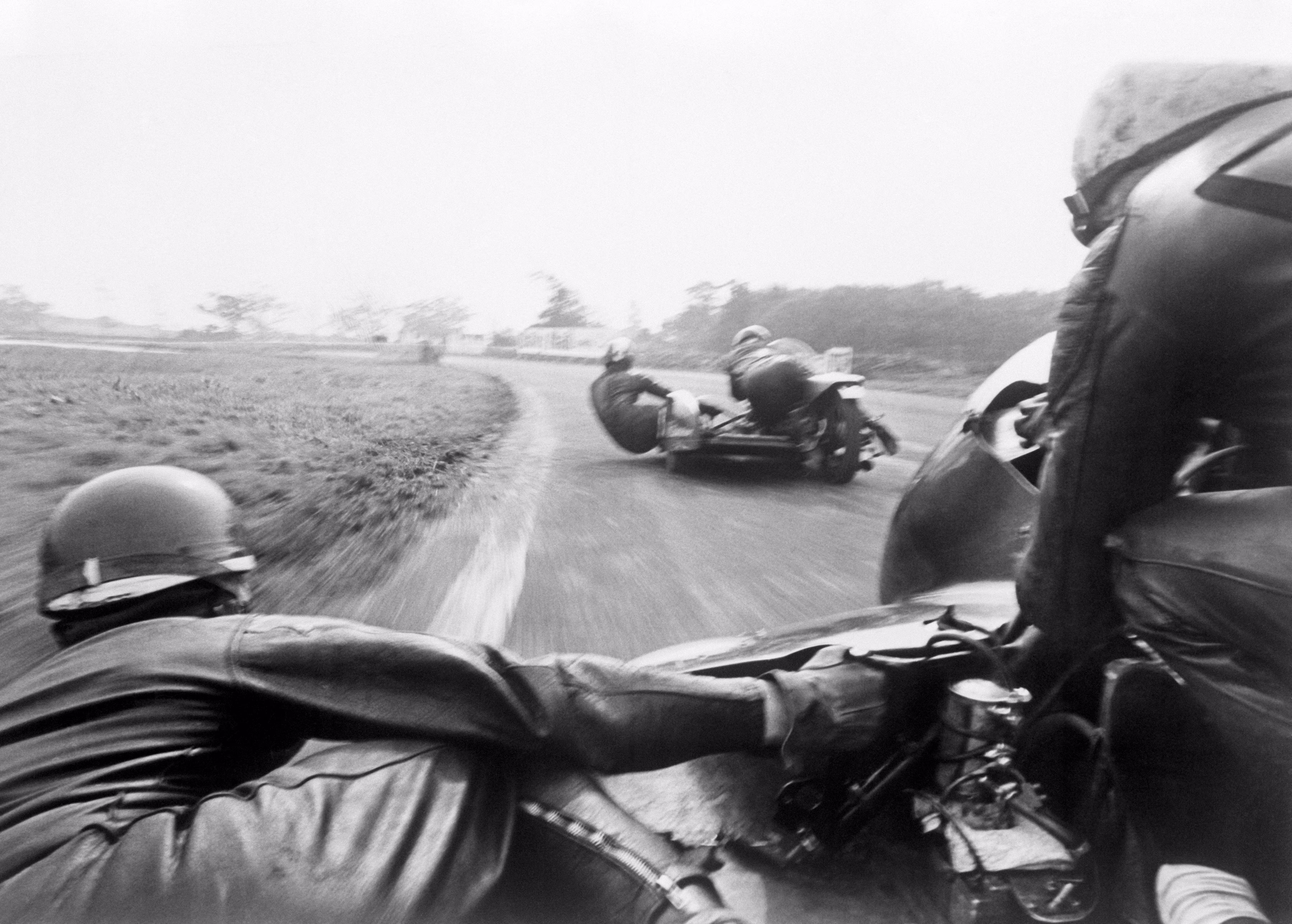 Two pairs of sidecar racers lean into a turn during a race in 1965.