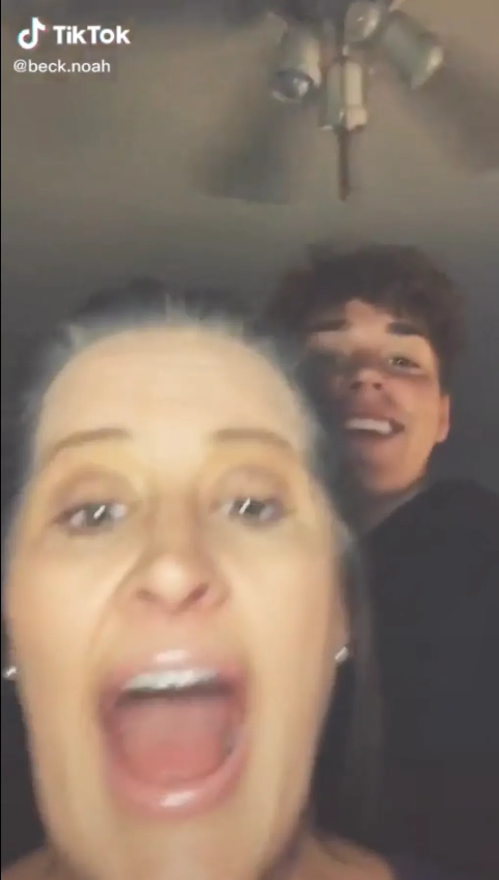 Amy Beck with her mouth wide open and a young man smiling behind her, presumably Noah Beck.