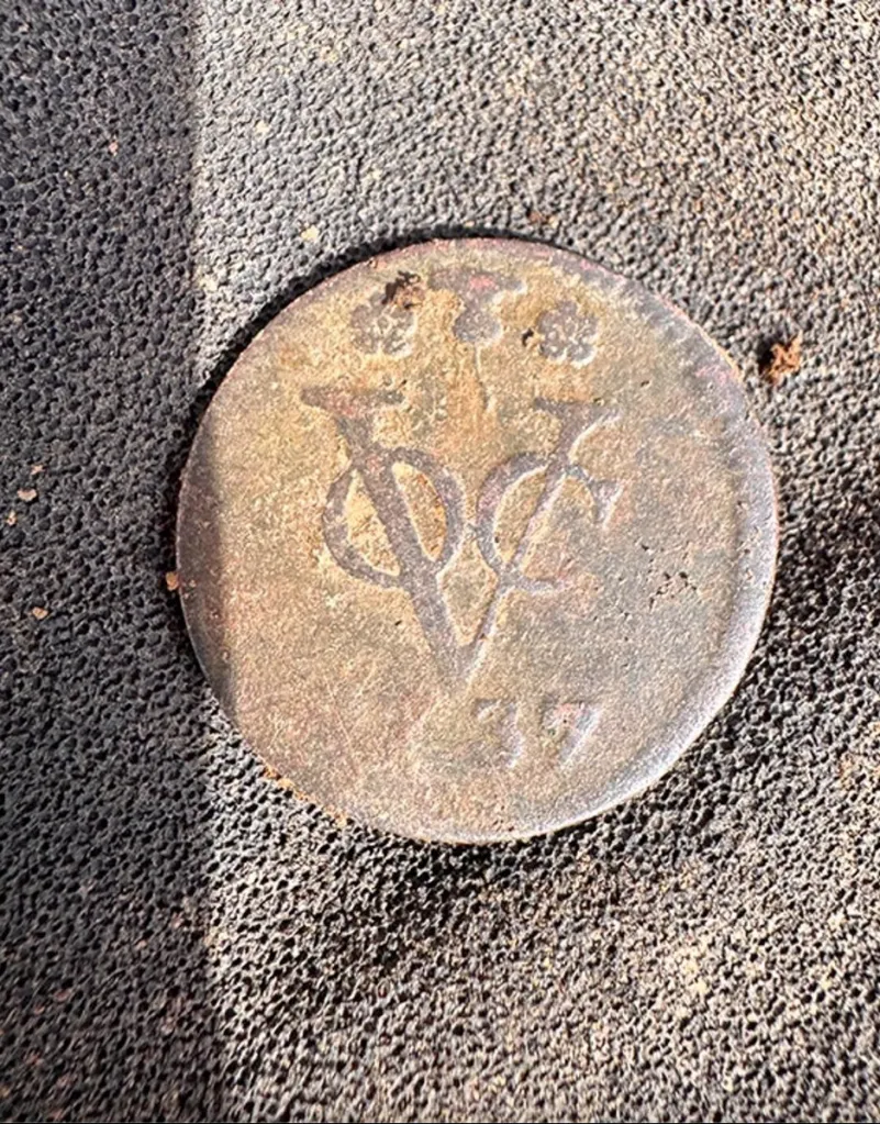 Close-up of an unearthed colonial-era coin with the letters "VC" and number "77" visible.