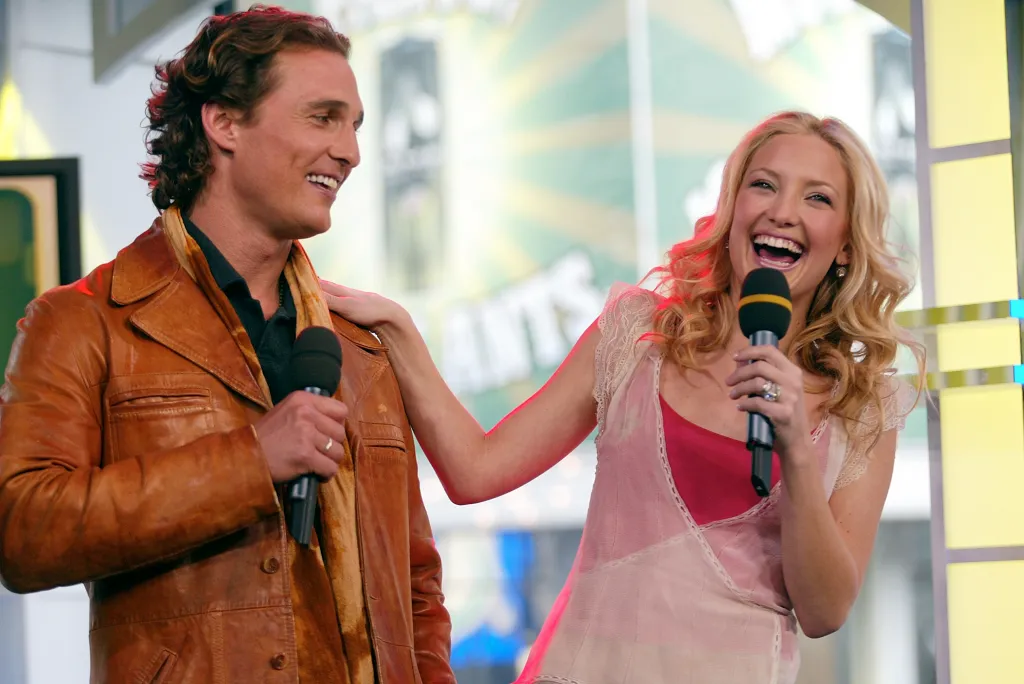 Kate Hudson and Matthew McConaughey laugh while holding microphones.