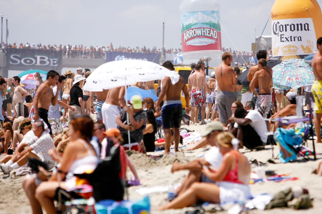 Large crowd of people on a beach with two large inflatable bottles for Arrowhead Mountain Spring Water and Corona Extra visible.