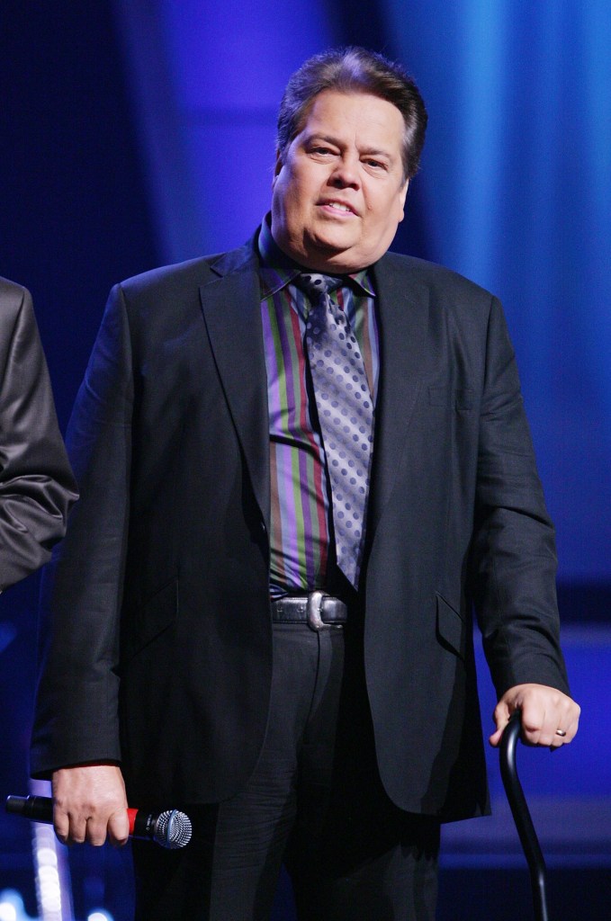 Entertainer Alan Osmond holding a microphone and a cane during a performance.