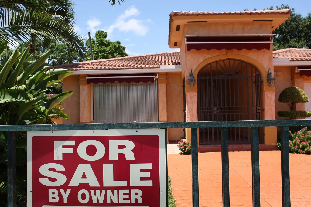A red "FOR SALE BY OWNER" sign in front of a Miami home.