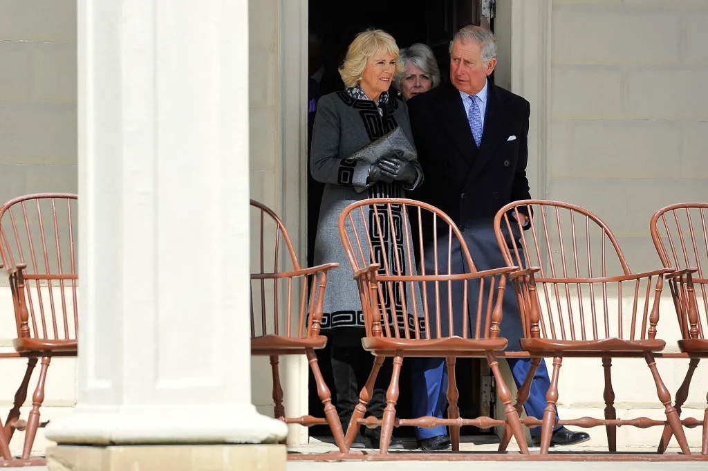 Prince Charles and Camilla, Duchess of Cornwall, stand behind brown wooden chairs.