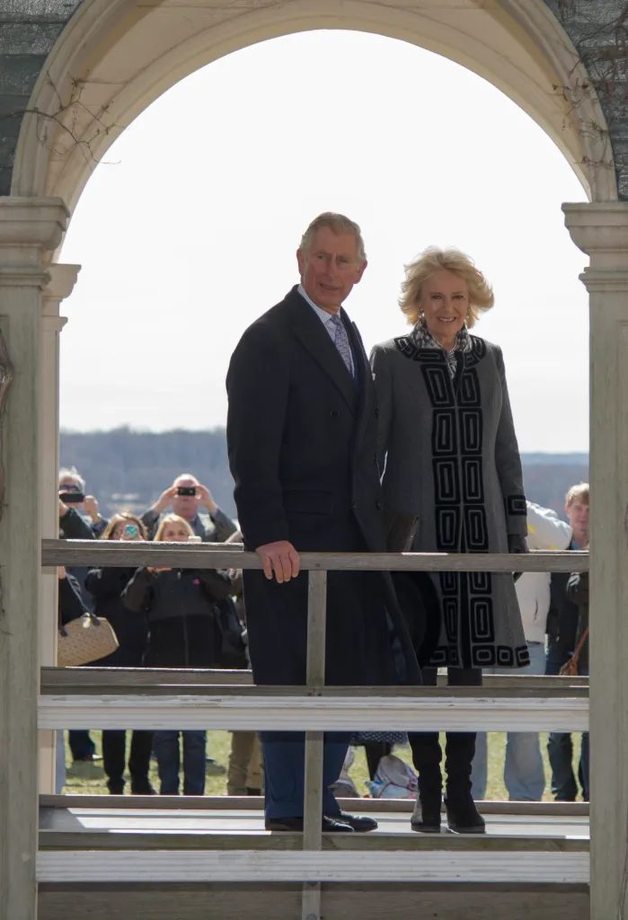 Prince Charles and Camilla, Duchess of Cornwall, standing in an arched gazebo, smiling at spectators.