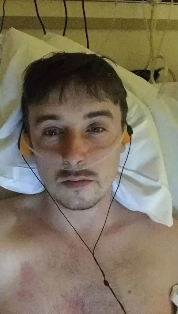 A young man with a nasal cannula and earbuds in a hospital bed.