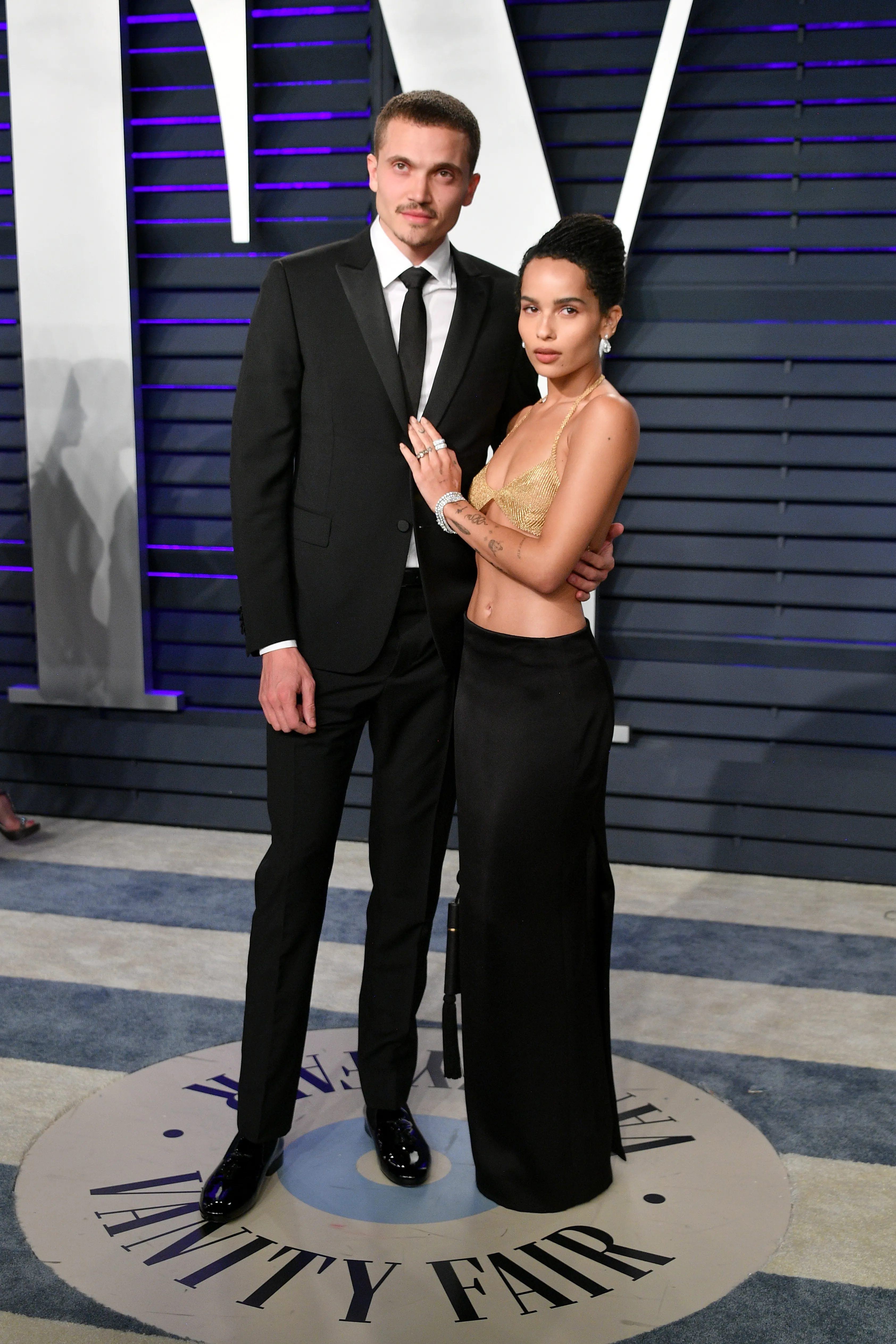 Zoe Kravitz in a gold mesh top and black skirt with Karl Glusman in a black suit.
