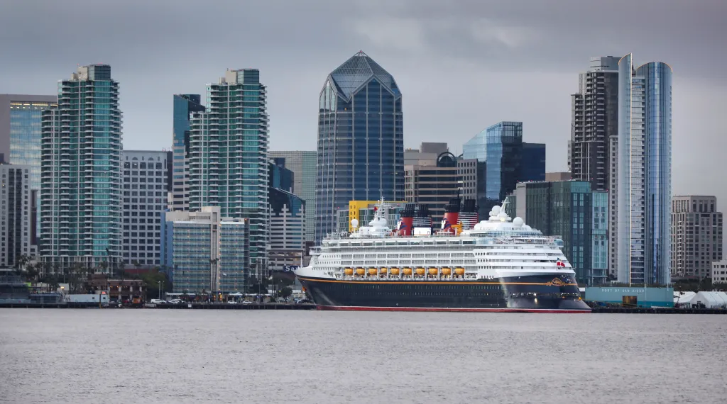 The cruise ship Disney Wonder docked in San Diego, California, with the city's skyline in the background.