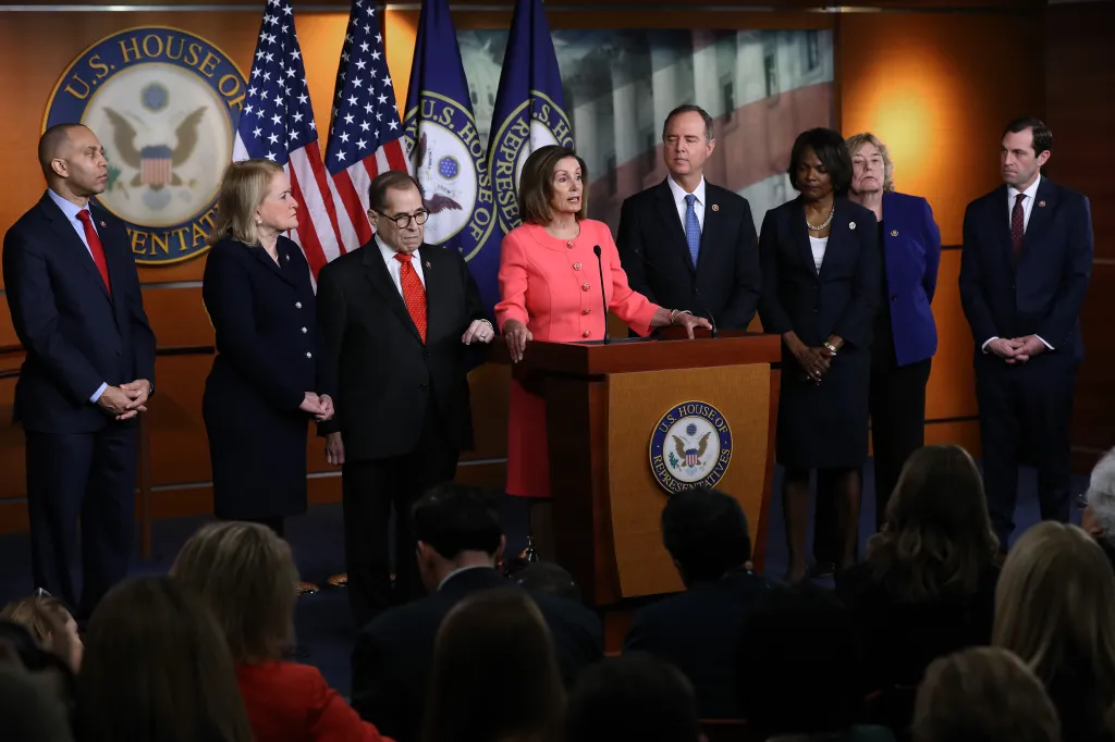 Speaker Nancy Pelosi announces impeachment managers at a podium in front of a U.S. House of Representatives seal, flanked by other representatives.