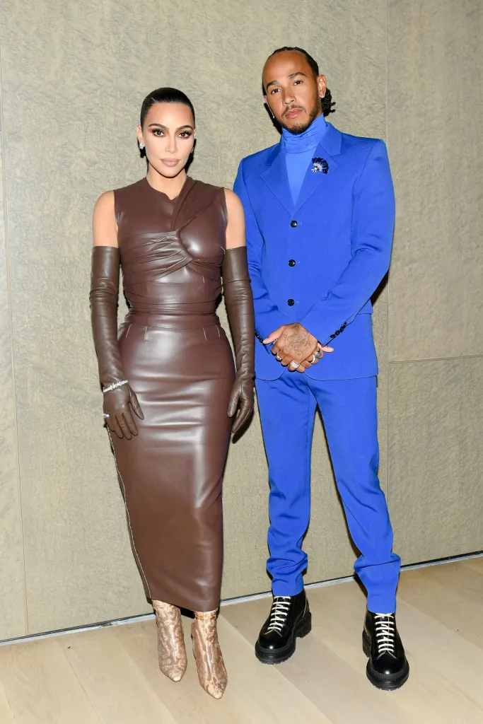 Kim Kardashian in a brown leather dress and Lewis Hamilton in a blue suit pose for a photo.