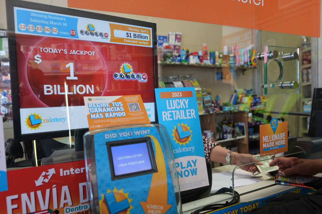 A display screen at a lottery retailer showing a $1 billion Powerball jackpot, with a customer buying tickets.