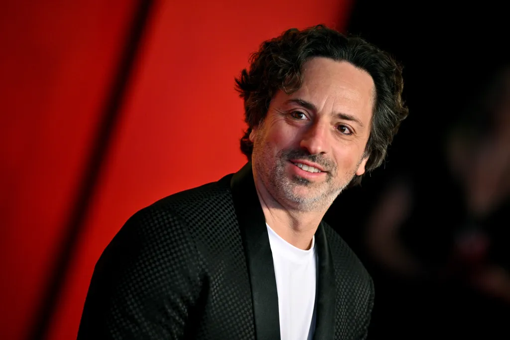 Sergey Brin smiling in a black textured blazer and white t-shirt.