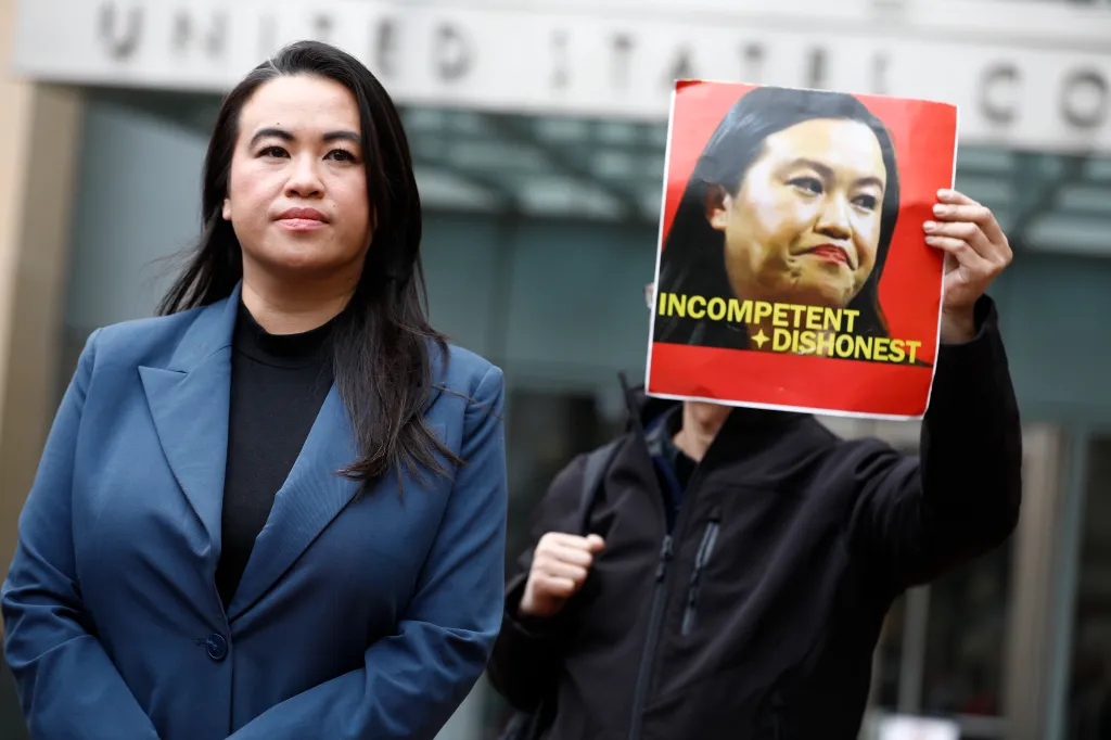 Former Mayor Sheng Thao outside the United States District Court addresses members of the news media as Tuan Ngo protests with a sign accusing her of being "incompetent + dishonest."