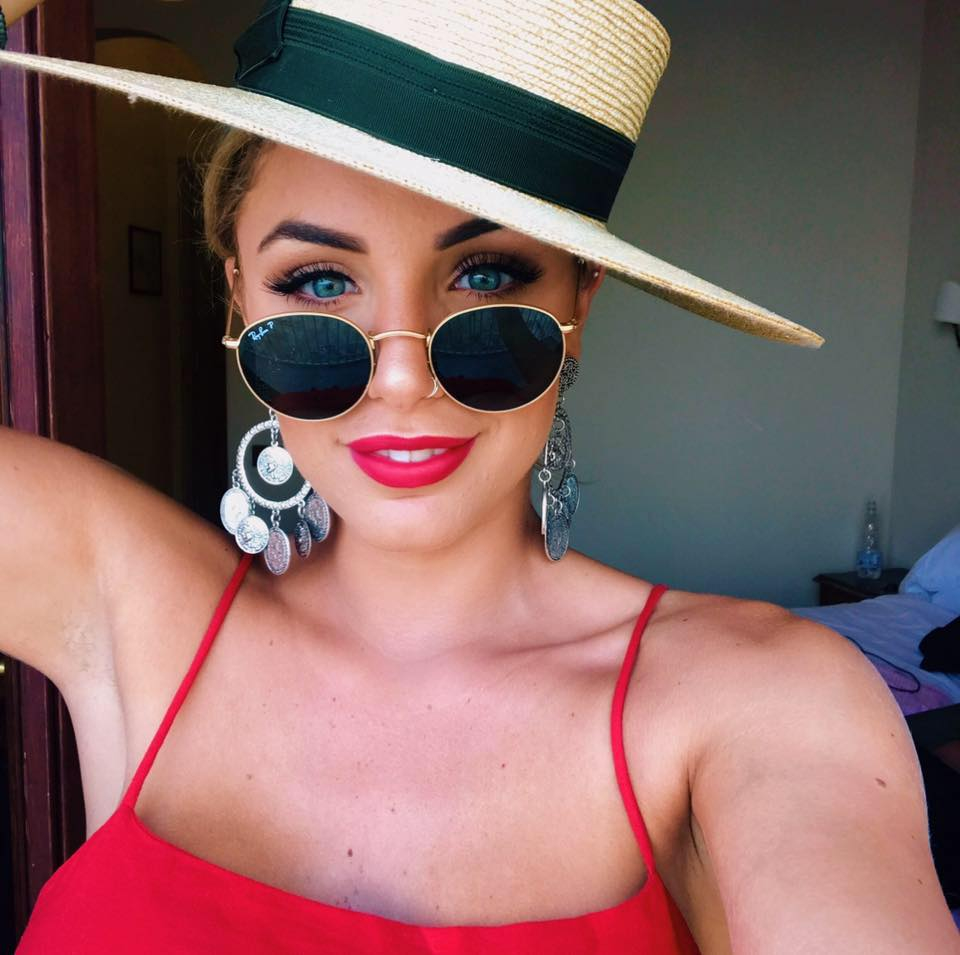 Delina Stevenson wearing a straw hat, sunglasses, a red top, and large earrings.